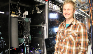 JILA graduate student Alexander Aeppli stands next to the strontium atomic clock in JILA and NIST Fellow Jun Ye's laboratory