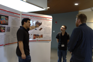 Two high school students explain to undergraduate Cameron Harres their research as part of the PISEC High School Poster Symposium